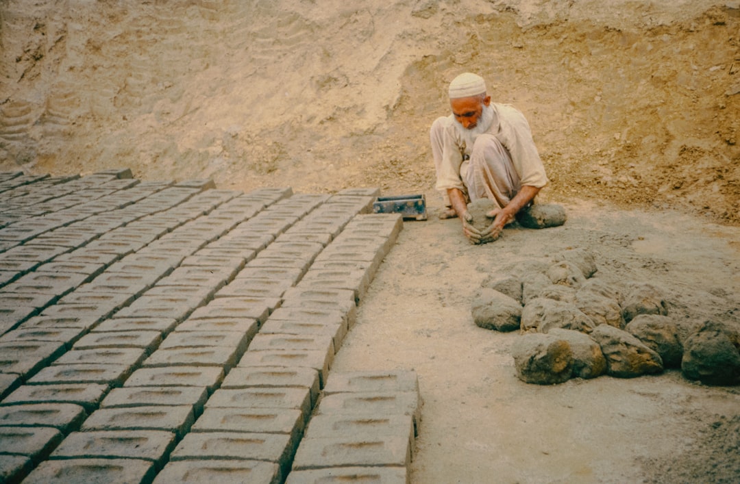 Un artisan qualifié agenouillé, en train de poser avec soin de grandes dalles de pierre grise sur un lit de mortier. Photographie par Scott Blake sur Unsplash.