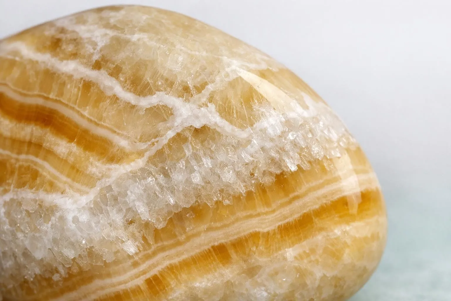 Extreme close-up photograph of polished onyx stone showing translucent honey-colored bands, white veining patterns, and crystalline microstructure under professional lighting against neutral background