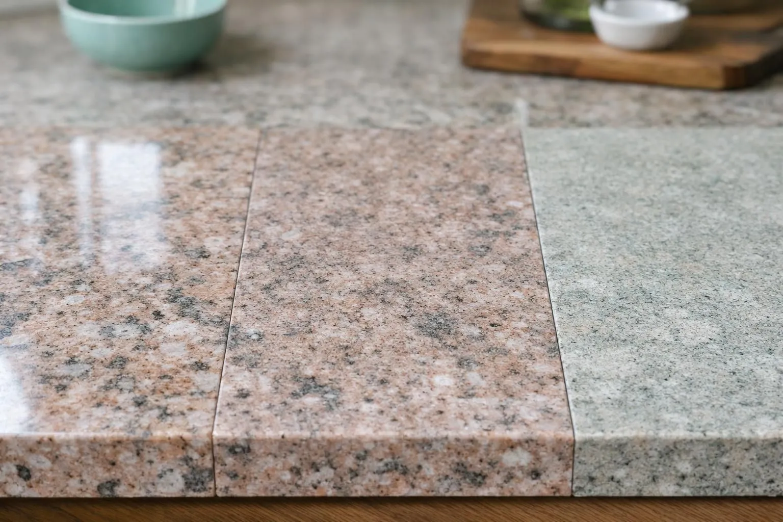 Close-up comparison of different granite finishes and colors showing polished, leathered and honed textures side by side on kitchen countertops with natural lighting highlighting the surface variations