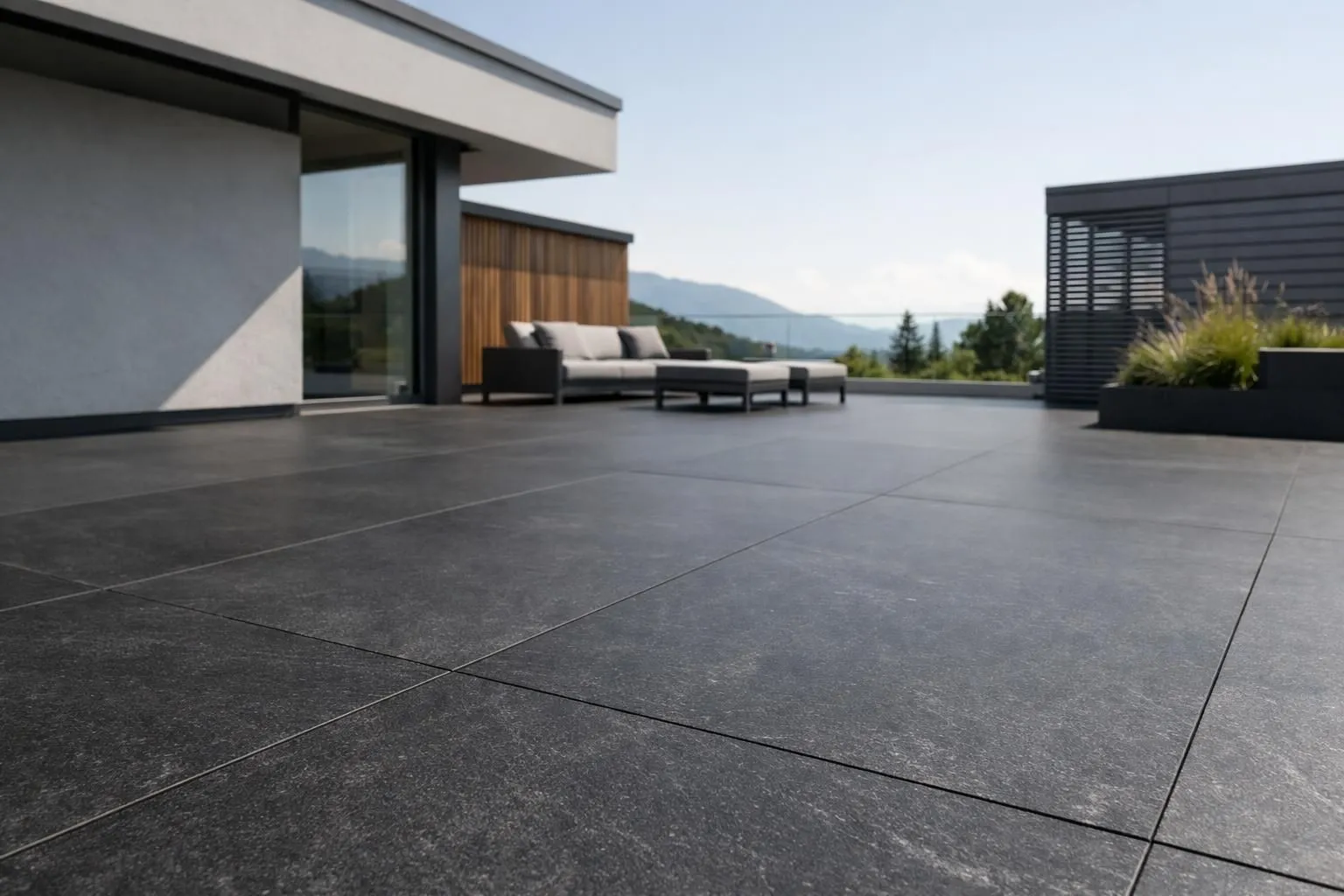 Large-format natural stone slabs (2×1m) installed on a modern minimalist terrace in Switzerland, showcasing smooth joints and dark anthracite finish under natural daylight, with clean architectural lines and sustainable Minergie-P construction elements visible in the background