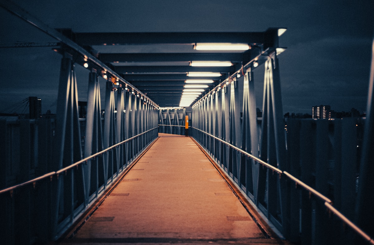 Passerelle métallique éclairée la nuit, menant à un bâtiment.