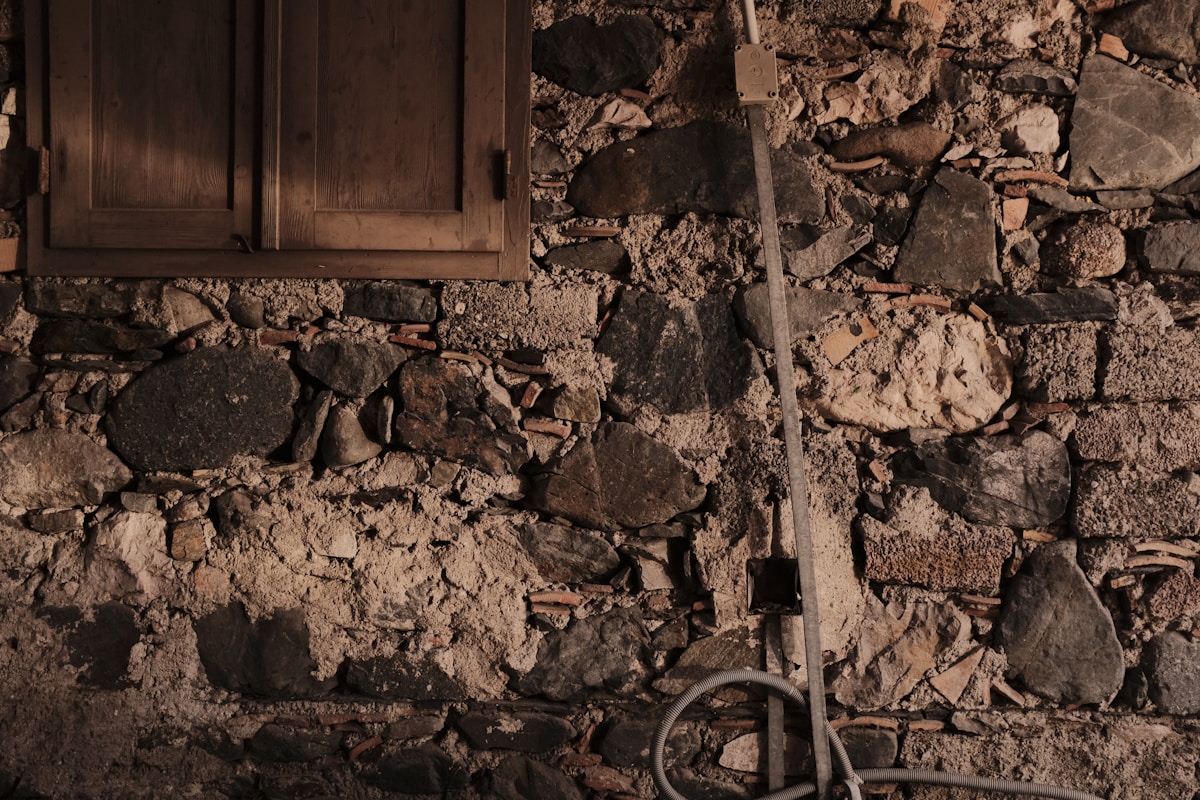 Mur de pierres rustique avec tuyau et débris au sol.