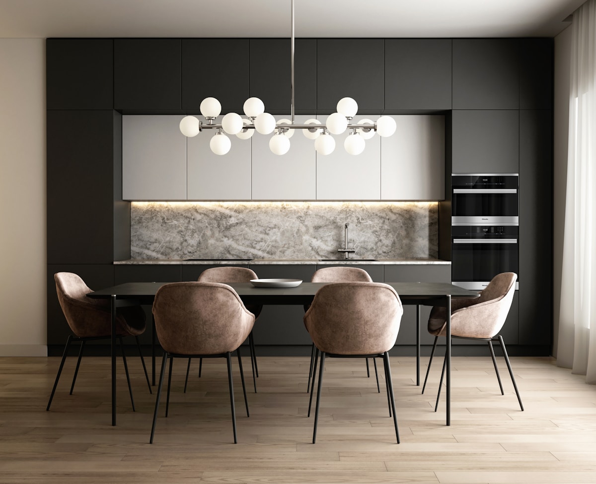Cuisine moderne avec meubles noirs, éclairage suspendu, et table à manger avec chaises en velours.