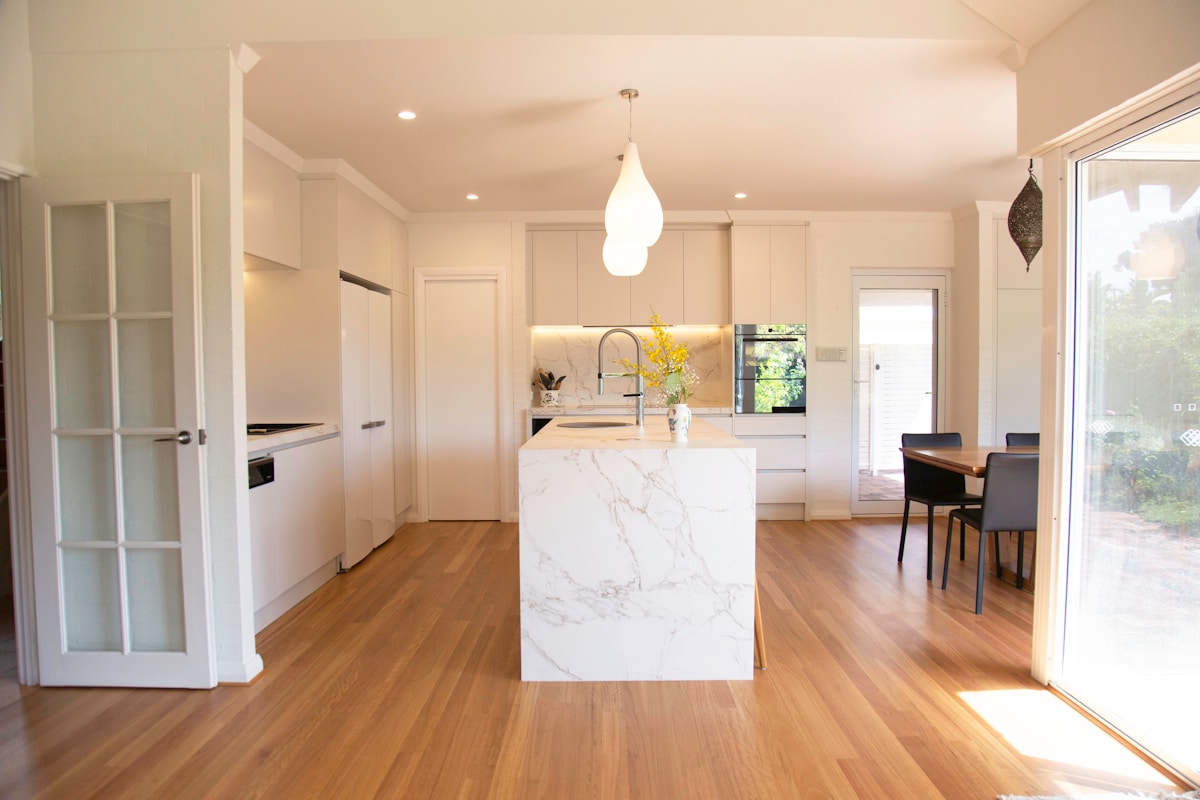 Cuisine moderne avec îlot en marbre blanc, luminaire suspendu et parquet en bois.