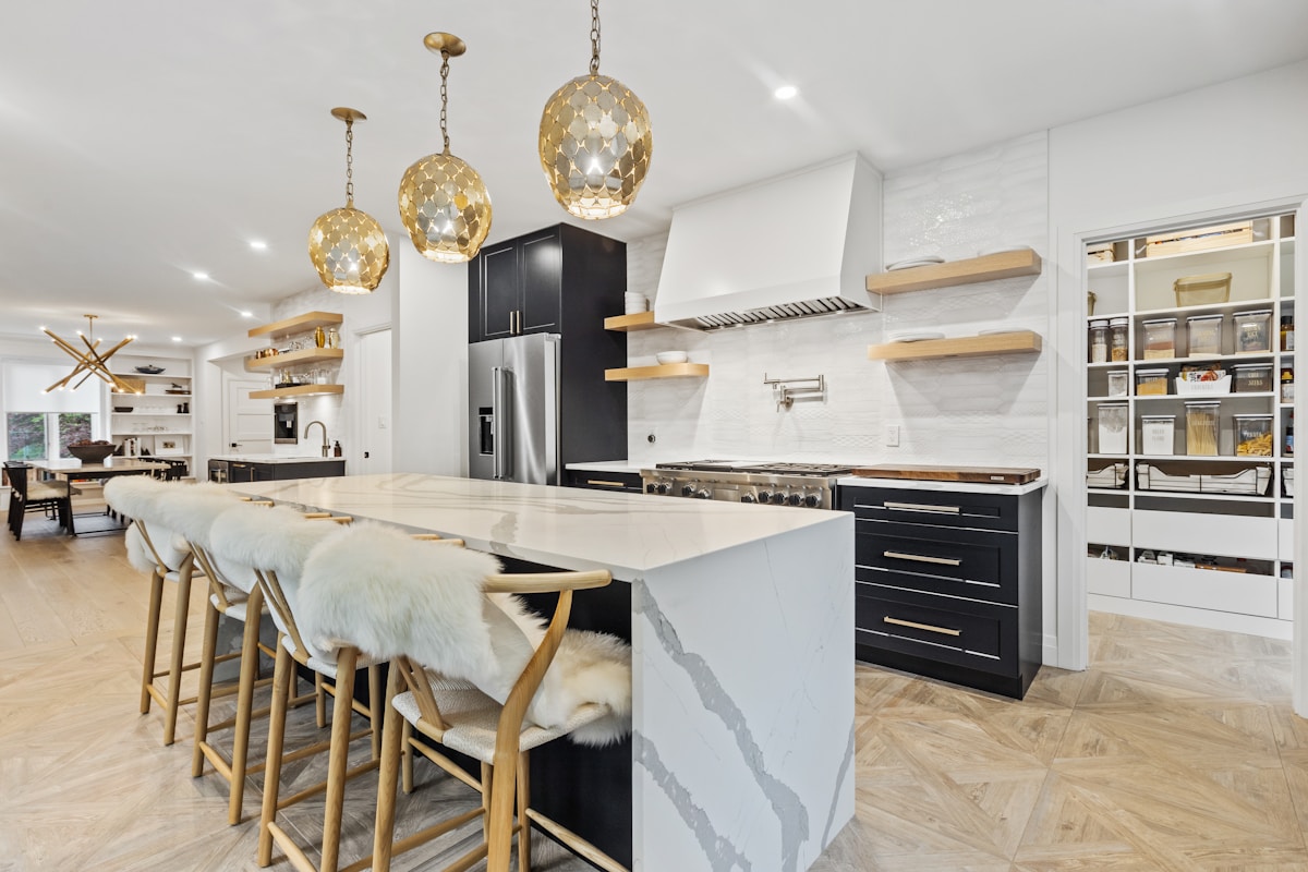 Cuisine moderne avec îlot central, luminaires dorés et électroménagers noirs.