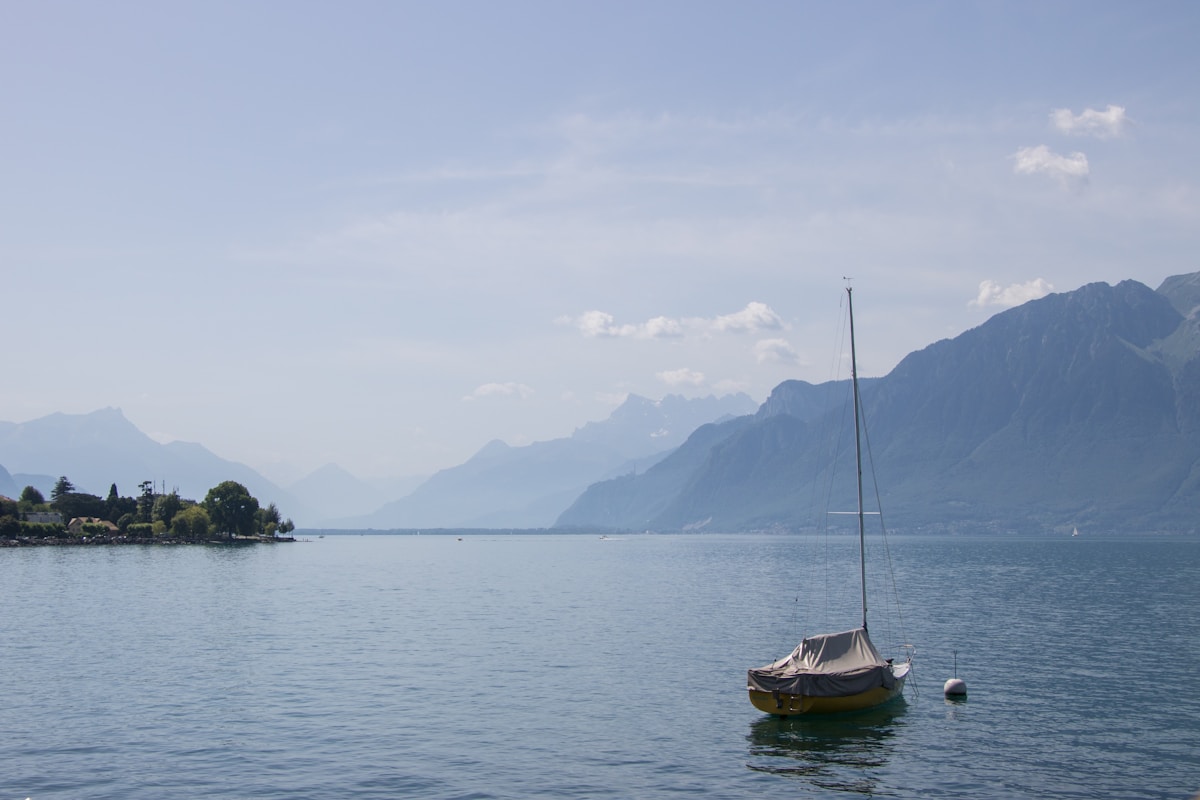 Paysage de montagne avec un bateau à voile sur un lac tranquille.