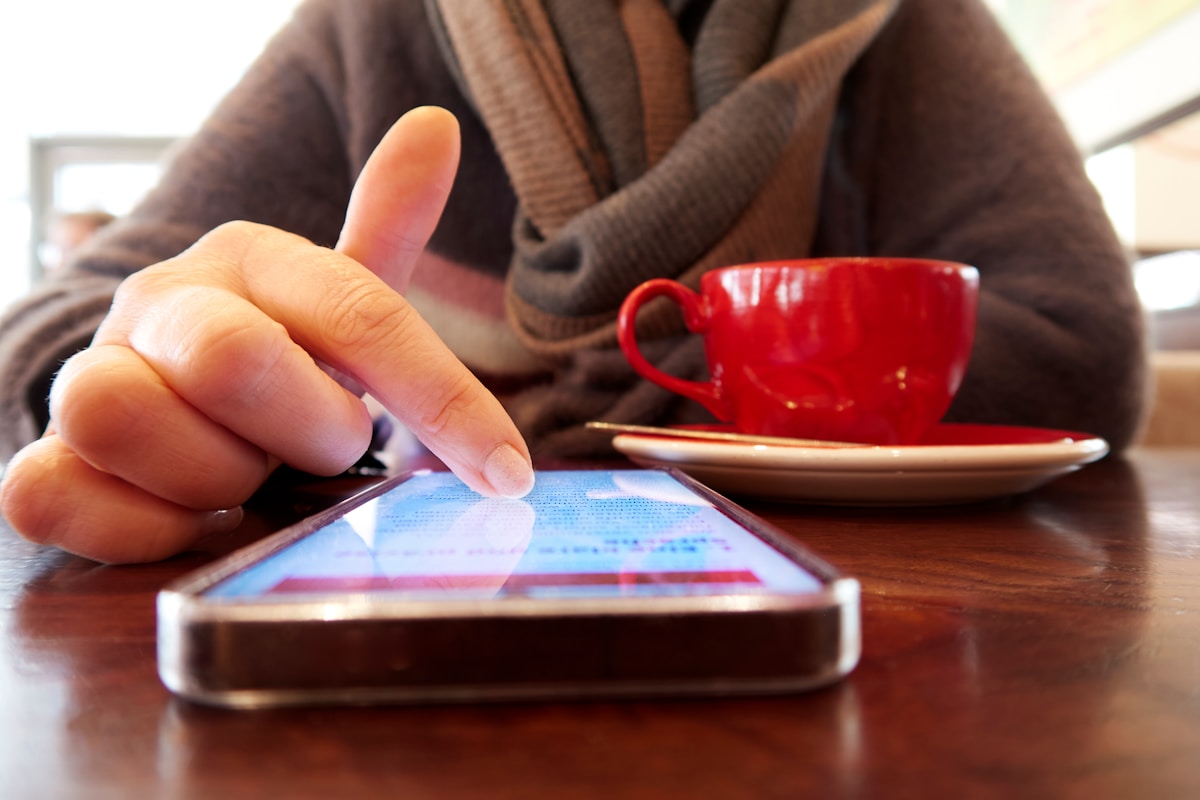 Personne utilisant un smartphone avec une tasse de café rouge sur la table.