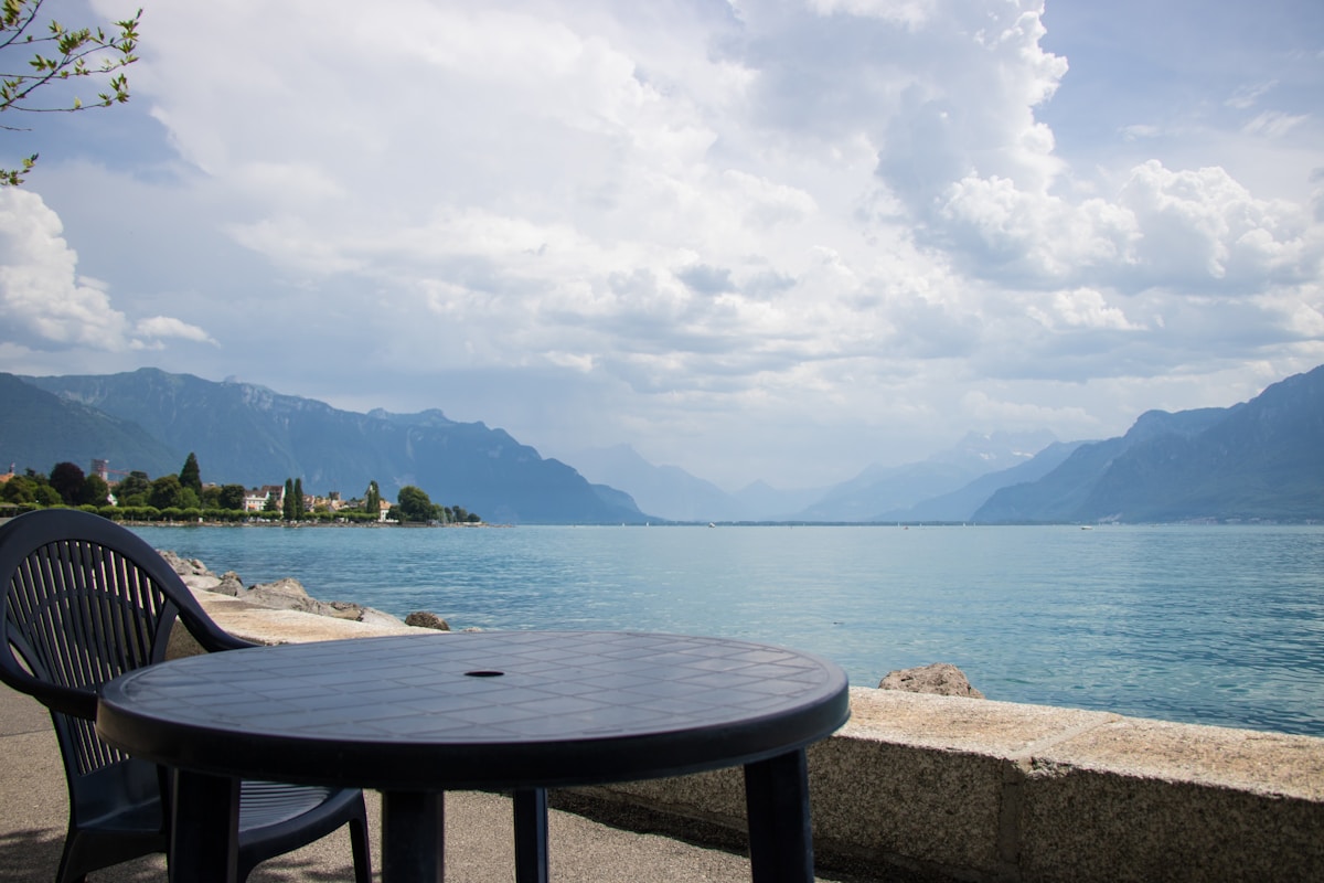 Paysage lacustre montagneux avec table et chaise sur la rive.