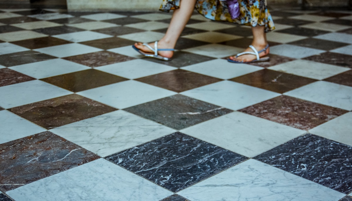 Carrelage de marbre noir et blanc, pieds en sandales sur le sol.