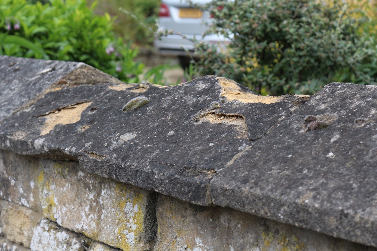 Mur de pierre grise et rugueuse avec des lichens jaunes.