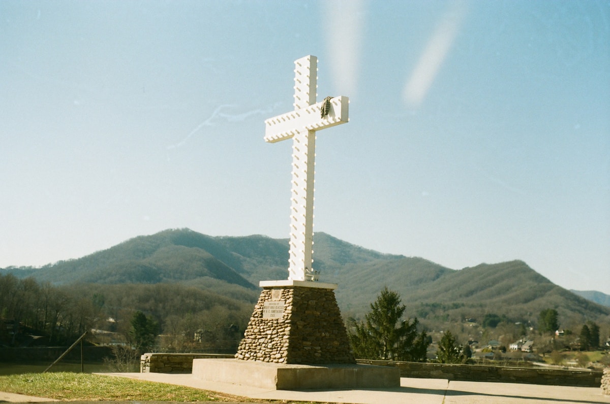Croix blanche sur un piédestal de pierre dans un paysage montagneux.