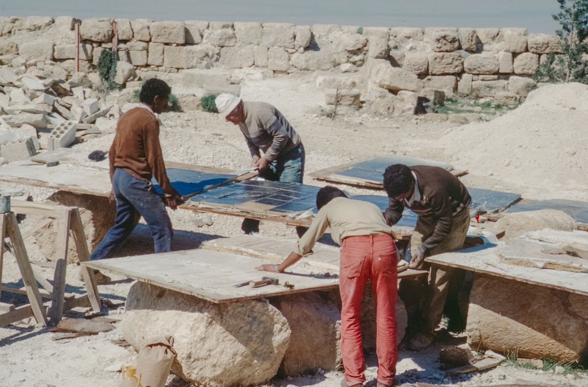 Groupe d'ouvriers construisant une structure en pierre dans un paysage désertique.