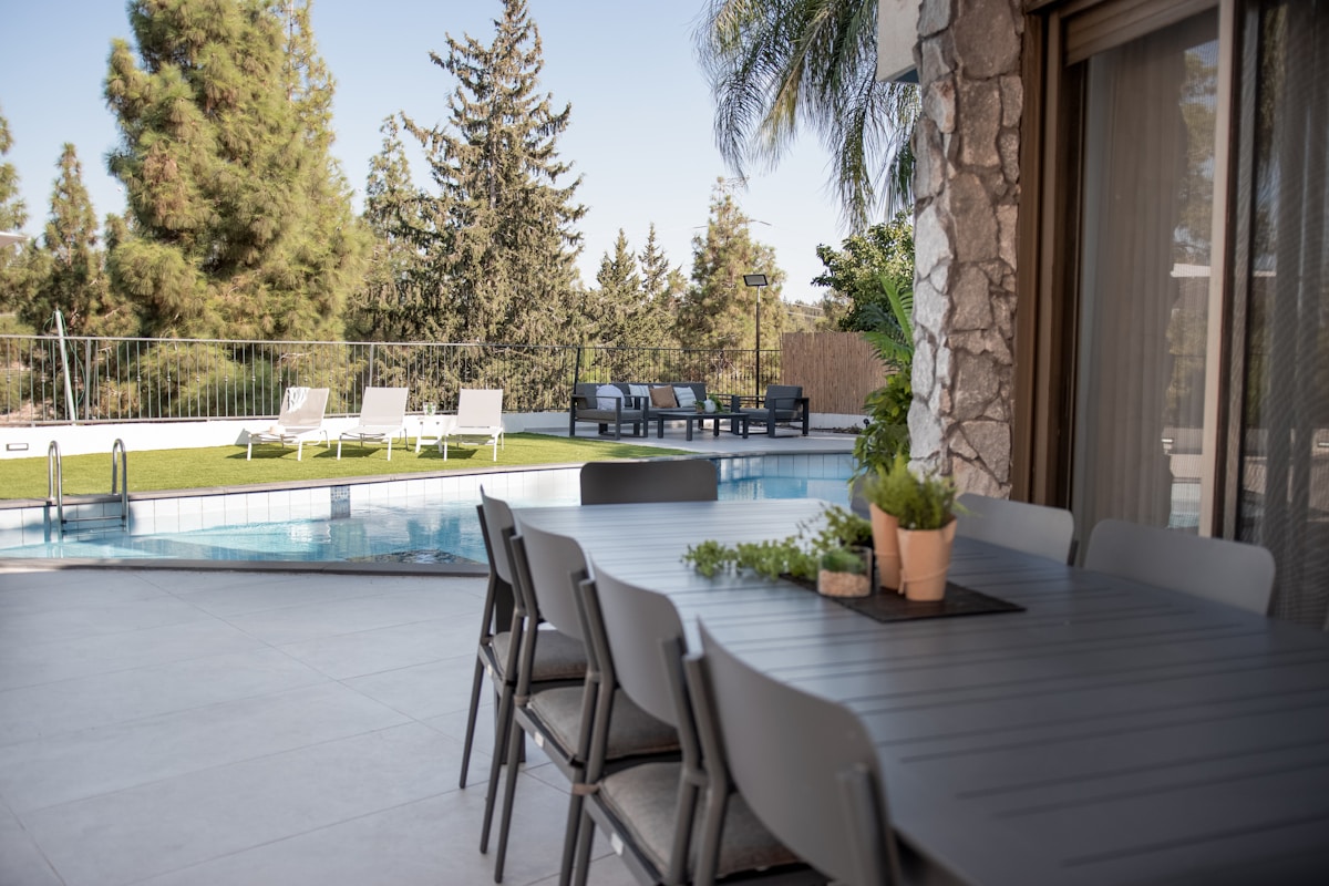 Piscine extérieure, terrasse, mobilier de jardin, arbres, végétation luxuriante.