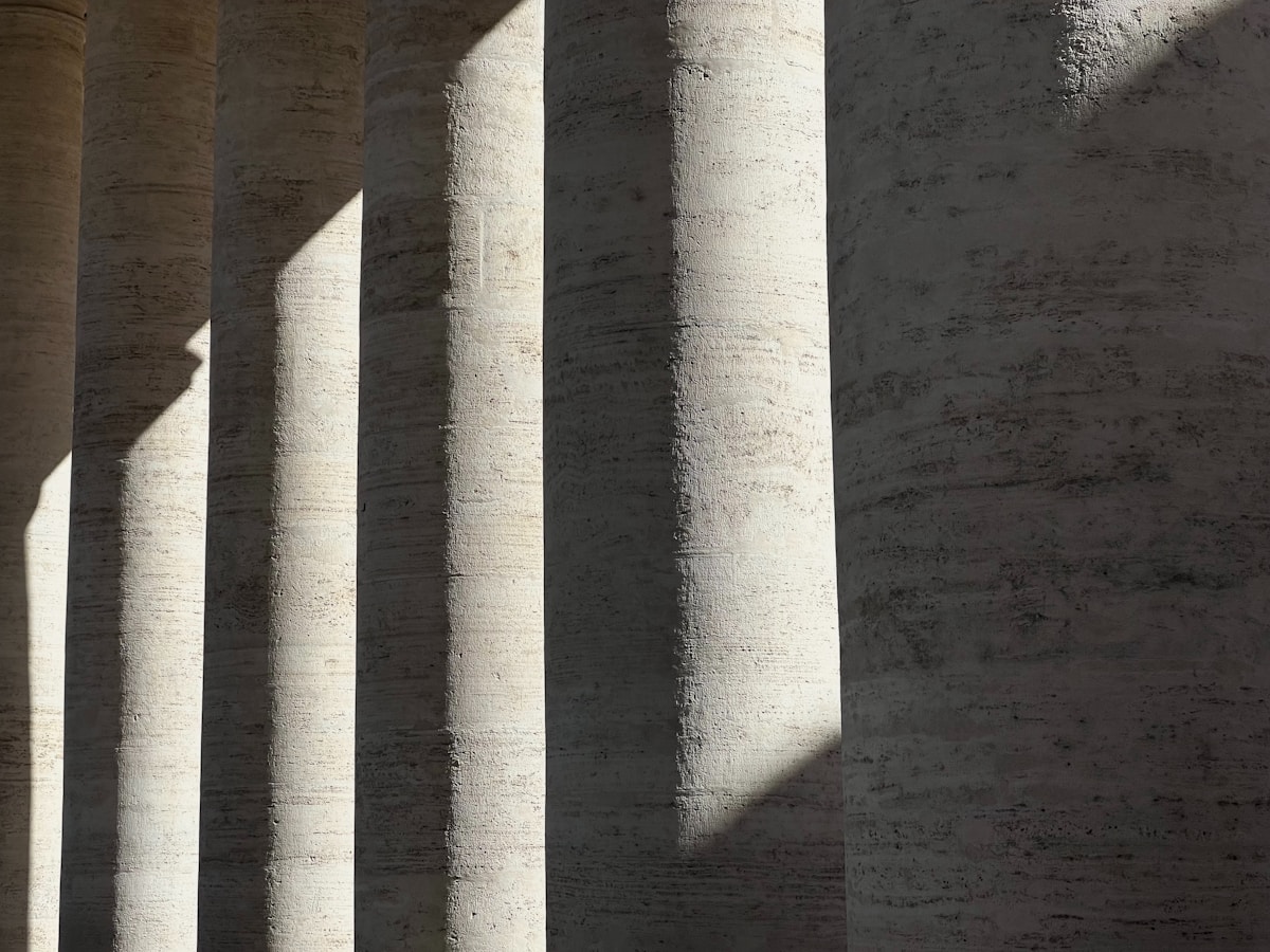 Colonnes de pierre blanche dans une ombre dramatique.