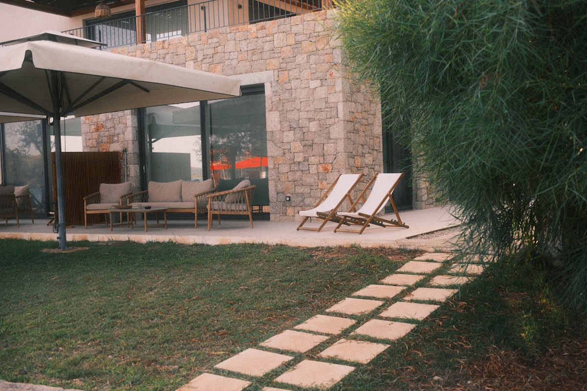 Terrasse extérieure avec meubles de jardin, allée de pierres et végétation luxuriante.