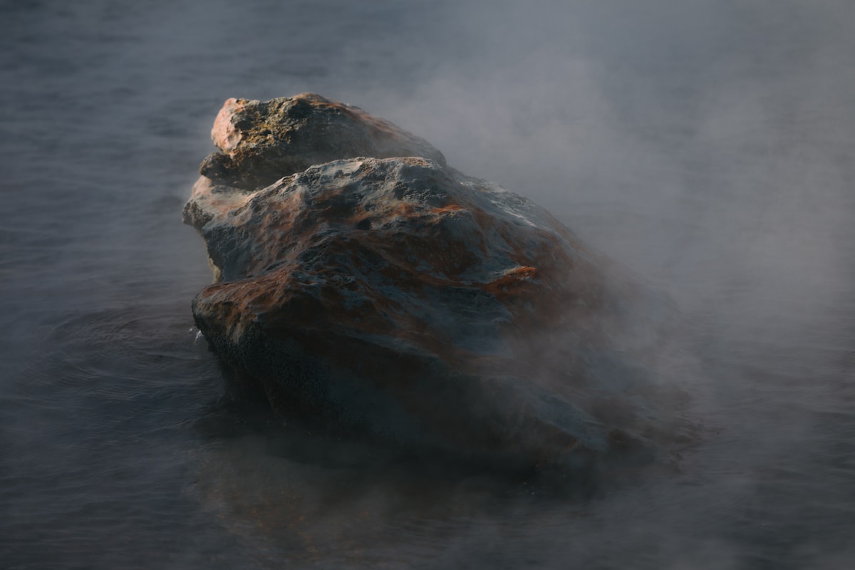 Rochers sombres et moussus émergeant de l'eau brumeuse.