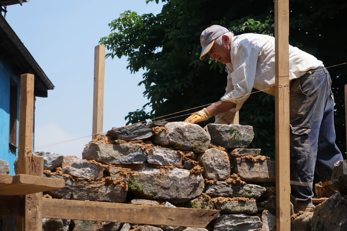 Homme en train de construire un mur de pierres dans un jardin.