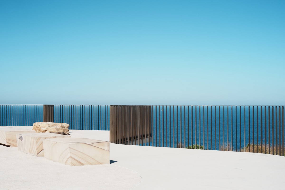 Terrasse avec vue sur l'océan, clôture en bois, rochers blancs.