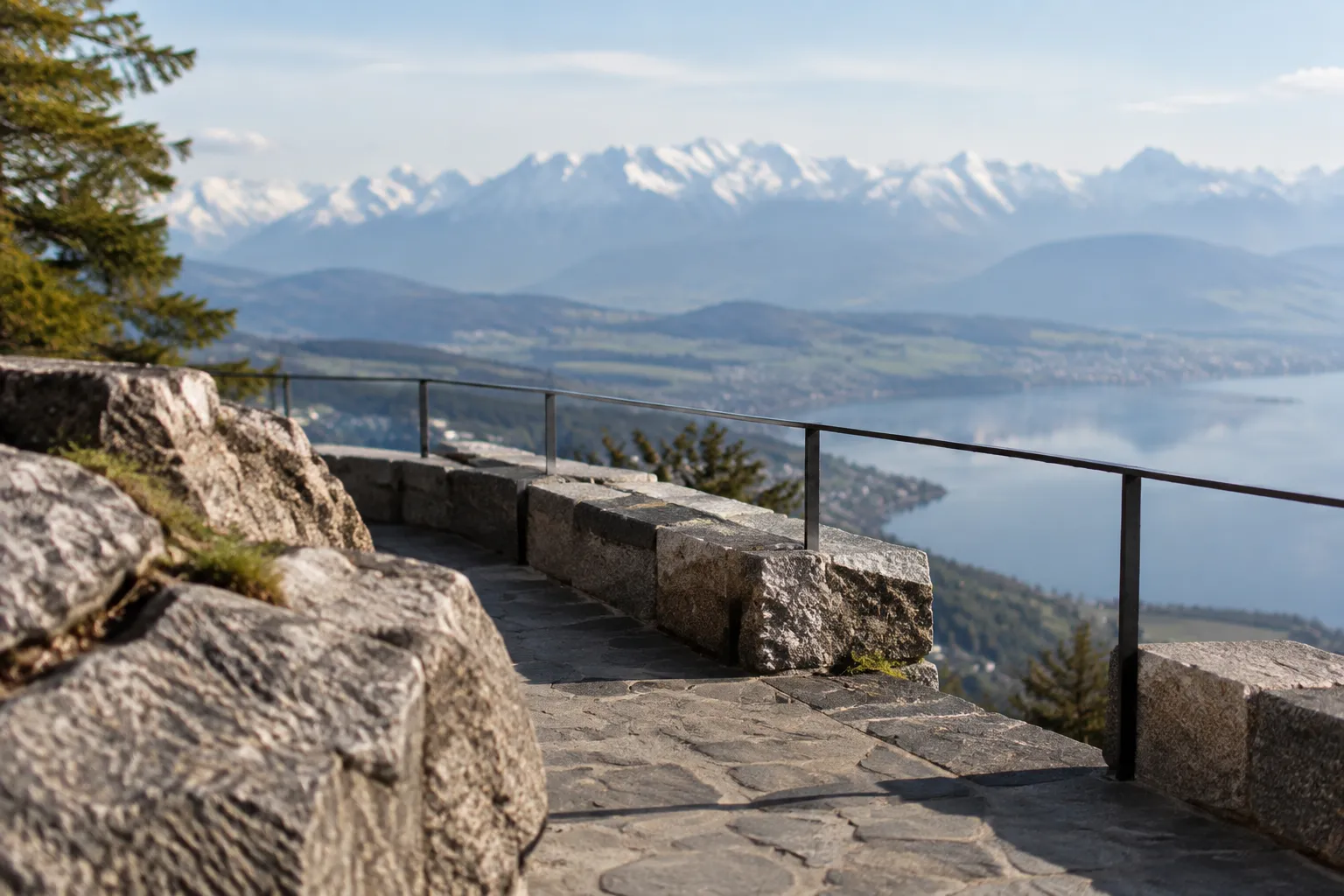 Terrasse en pierre naturelle au bord de l’Uetliberg avec les Alpes suisses en arrière‑plan flou.